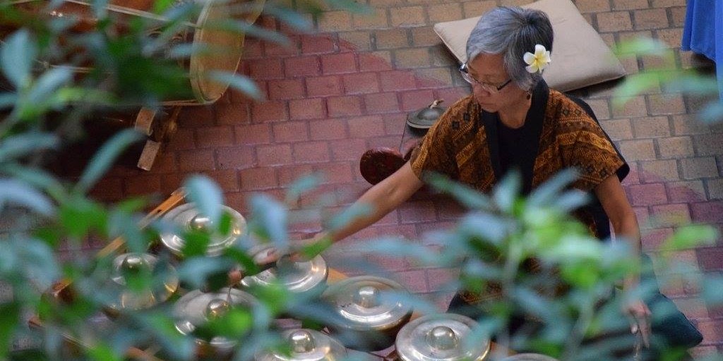Candid shot from behind leaves of performer playing on bonangs